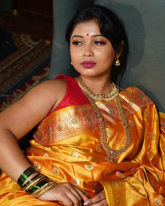 Woman in a traditional yellow saree with gold patterns, wearing jewelry, on a dark background.