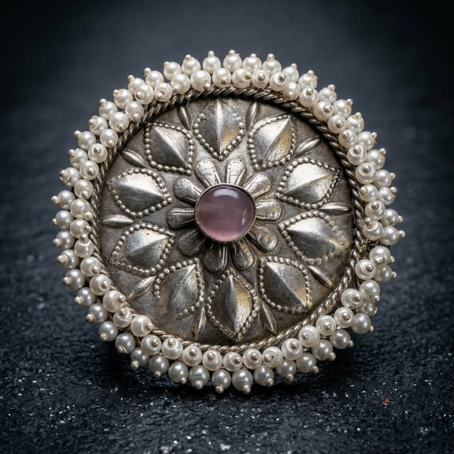 Decorative silver brooch with pearls and a purple gemstone on a dark background