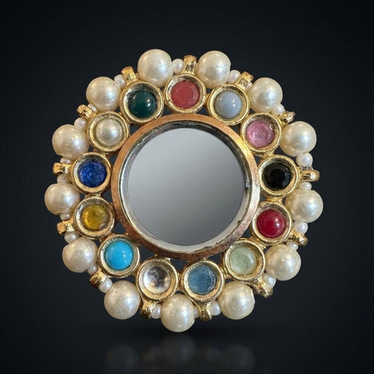Round mirror with pearl and gemstone frame on a black background