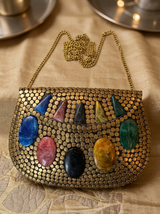Gold handbag with colorful stones on a textured surface