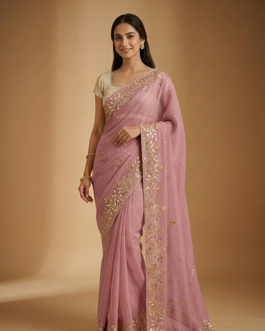 Woman wearing a pink saree with gold embroidery on a beige background