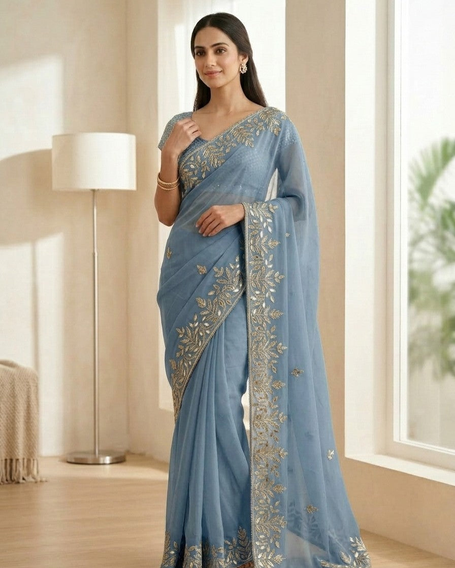 Woman wearing a light blue saree with silver embroidery in a room.