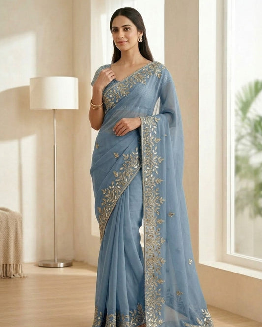 Woman wearing a light blue saree with silver embroidery in a room.