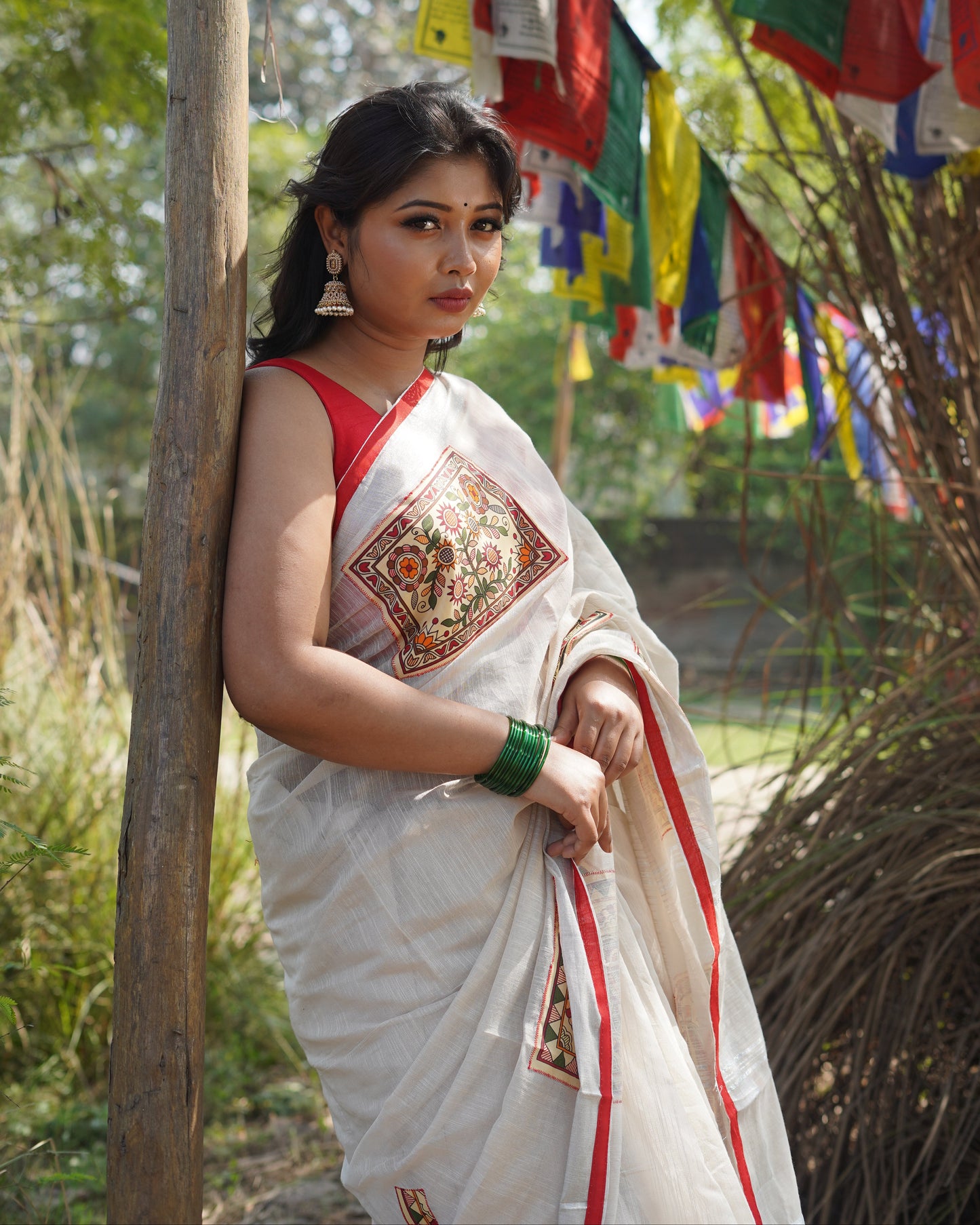Woman in traditional attire standing among colorful prayer flags with a natural background