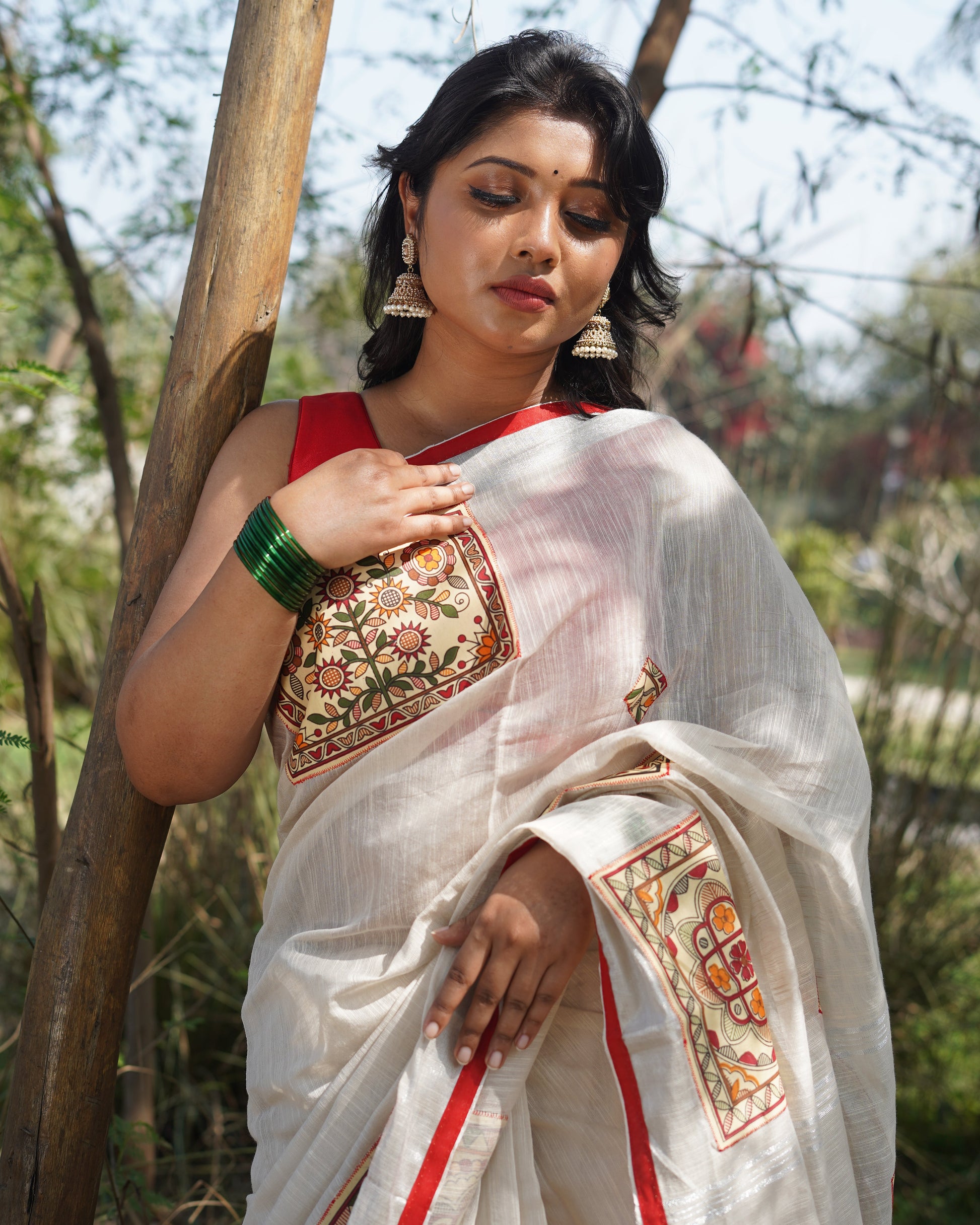 Woman in traditional attire standing outdoors with trees in the background