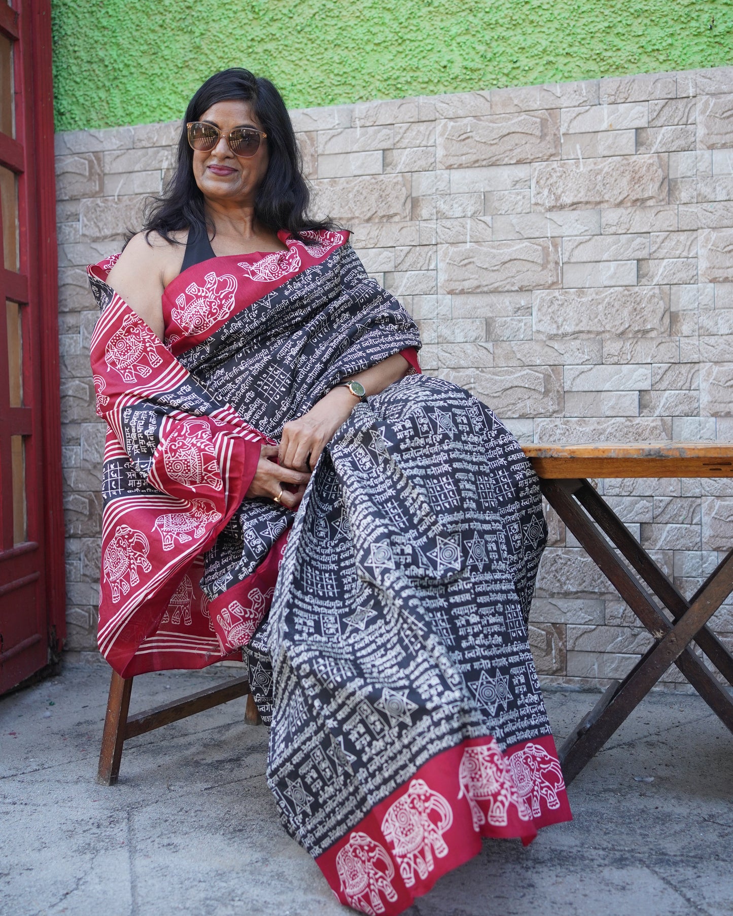 Woman sitting on a chair with a traditional patterned cloth draped over her, in an outdoor setting.