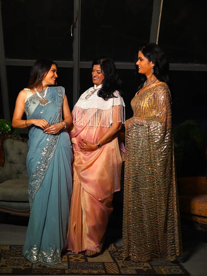 Three women in traditional sarees standing together indoors.