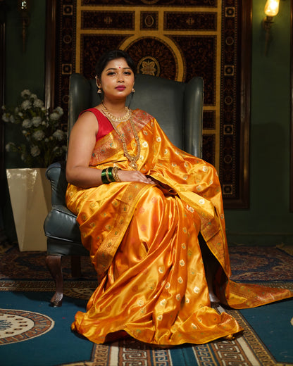 Woman in a yellow saree with a red blouse standing in an ornate room.