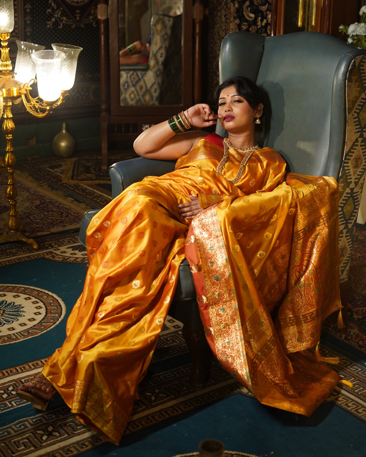 Woman in a yellow saree lying on a couch in an ornate room.
