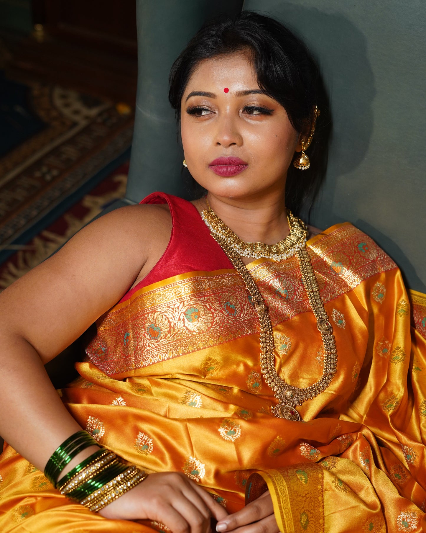 Woman in a traditional yellow saree with gold patterns, wearing jewelry, on a dark background.