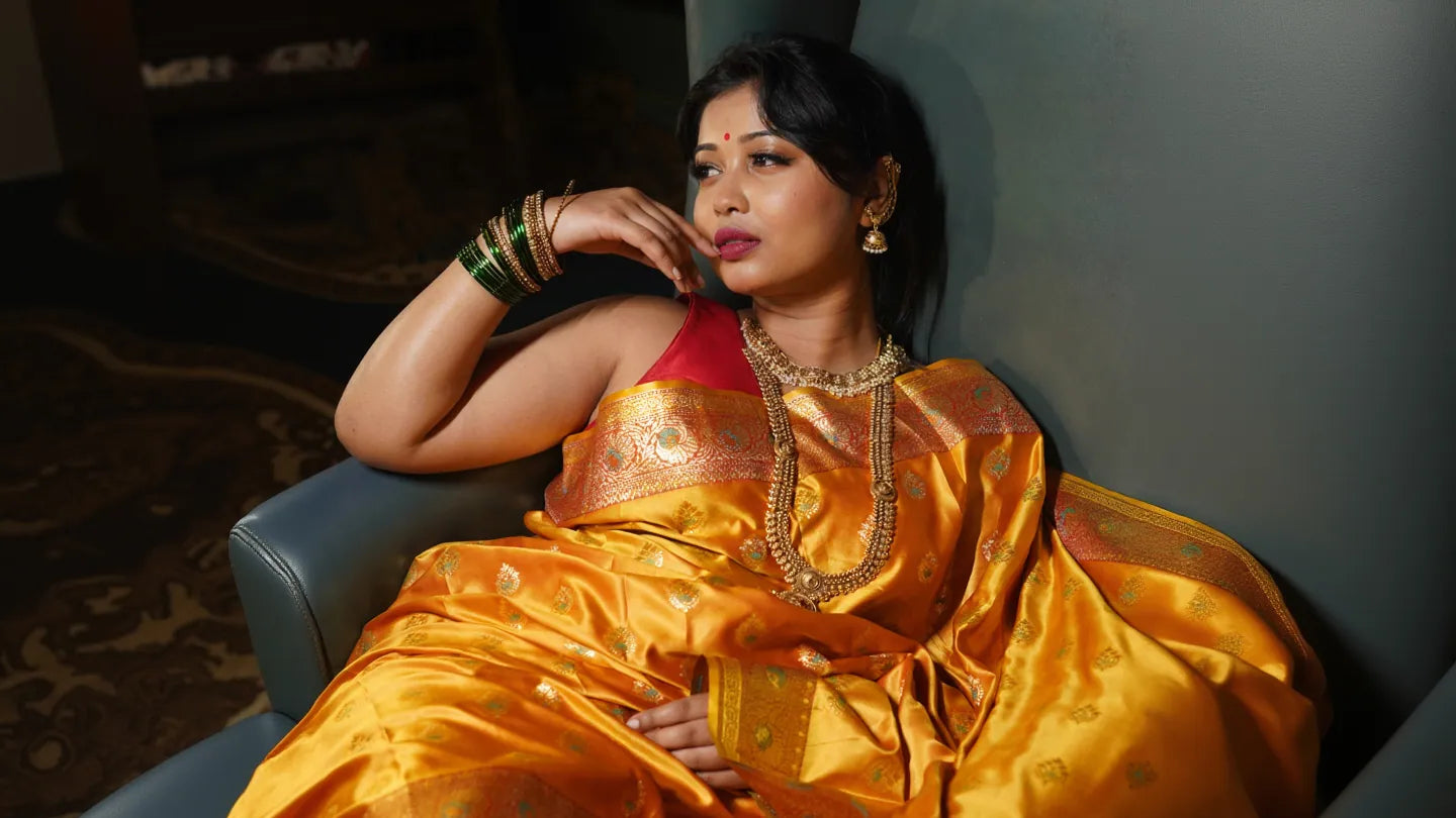 Woman in a traditional yellow saree with gold patterns lying on a dark surface.