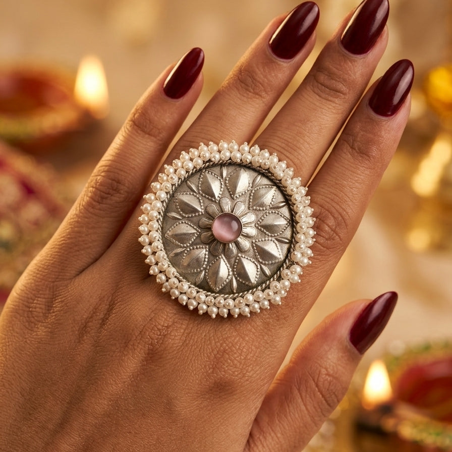 Decorative ring with pearl details on a hand against a warm, blurred background