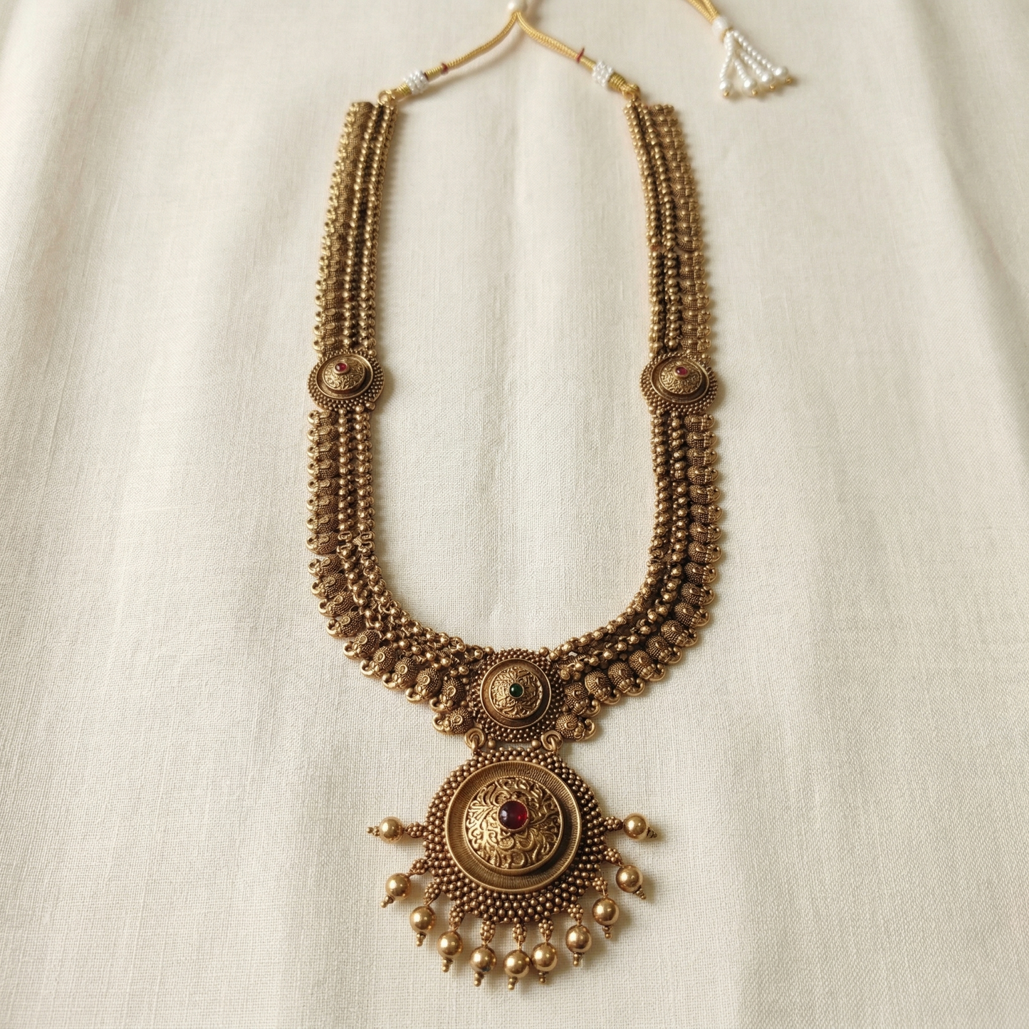 Decorative gold necklace with intricate designs on a light background