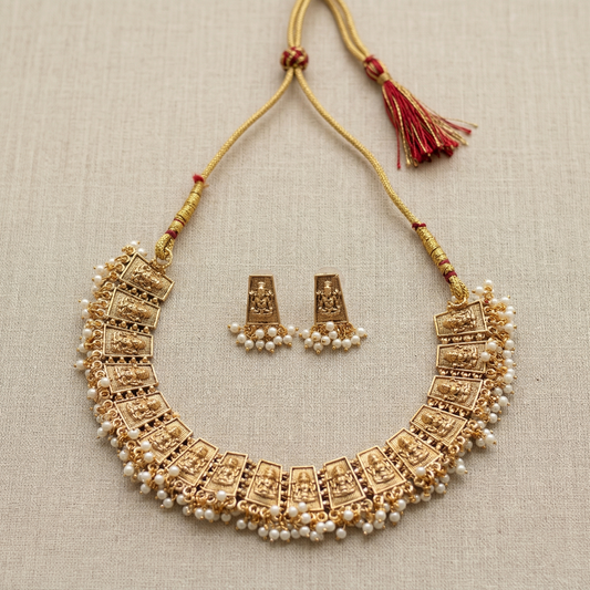 Gold necklace with pearl accents and matching earrings on a beige fabric background