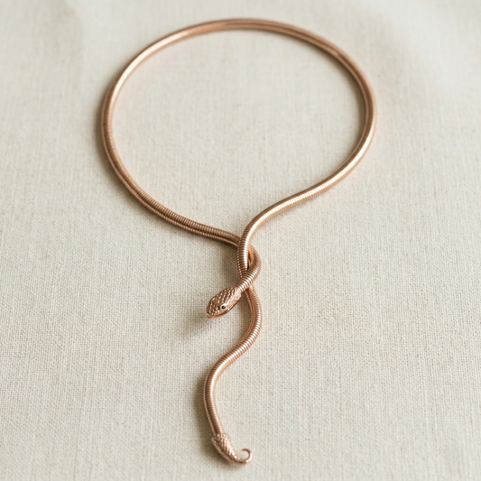 Rose gold snake necklace on a light beige fabric background