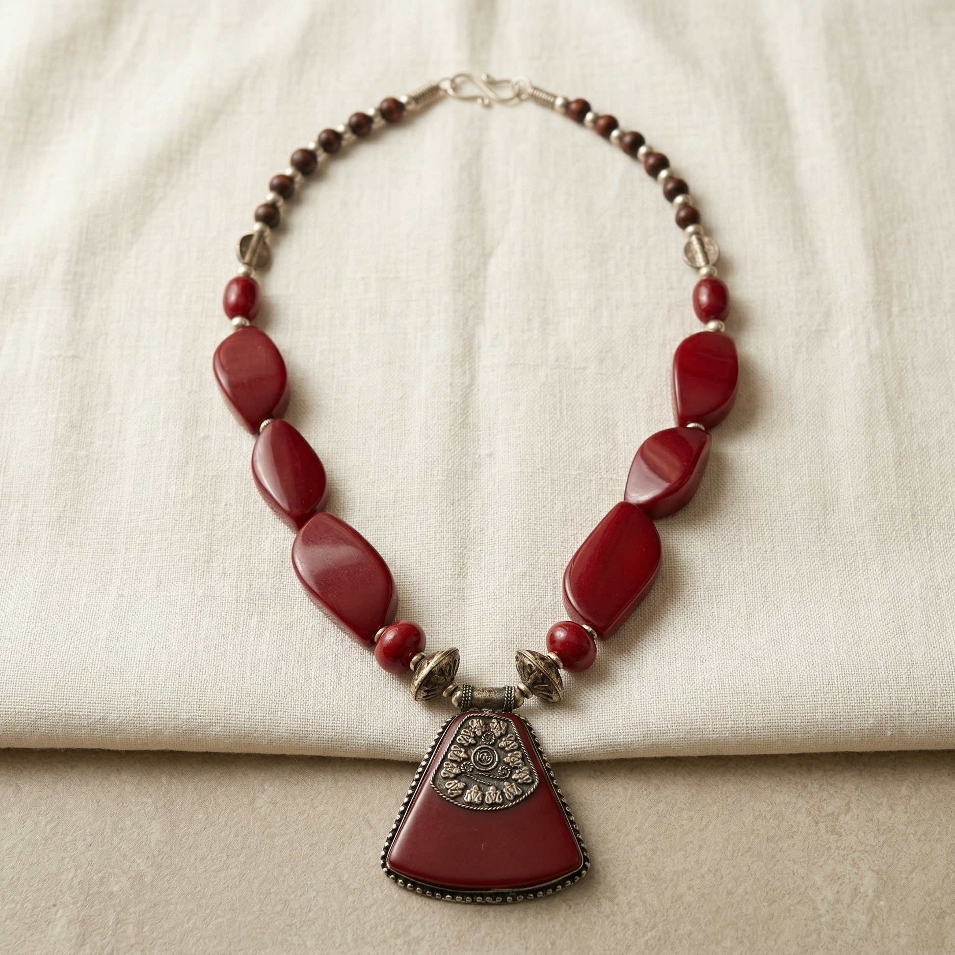 Necklace with red beads and a large pendant on a beige fabric background