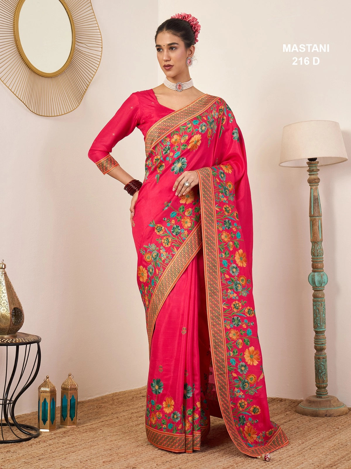 Woman wearing a bright pink saree with floral patterns in a room setting.