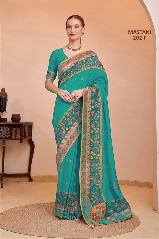 Woman wearing a teal saree with gold and multicolor patterns, standing against a beige wall.