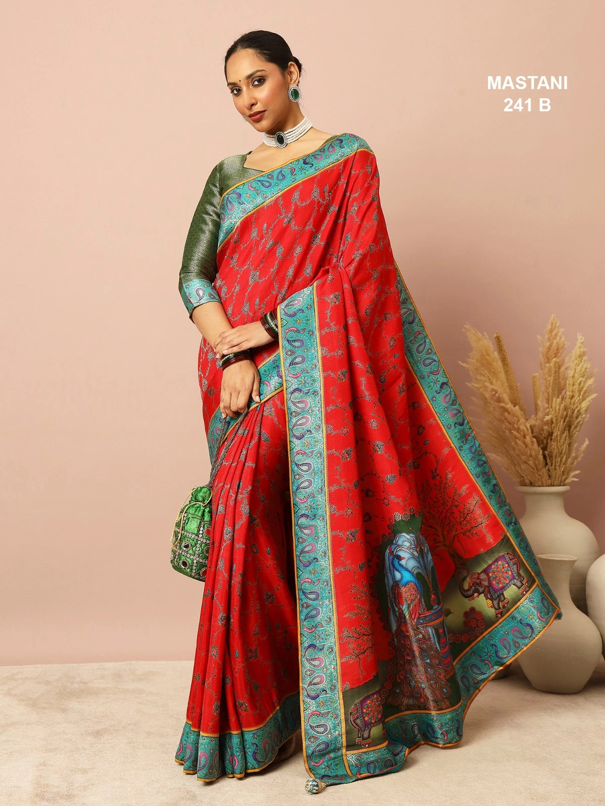 Woman wearing a red saree with green and blue border, holding a green bag against a beige background.