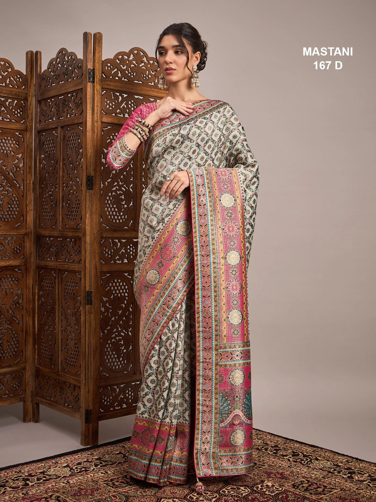 Woman wearing a traditional saree with intricate patterns in front of a wooden screen.