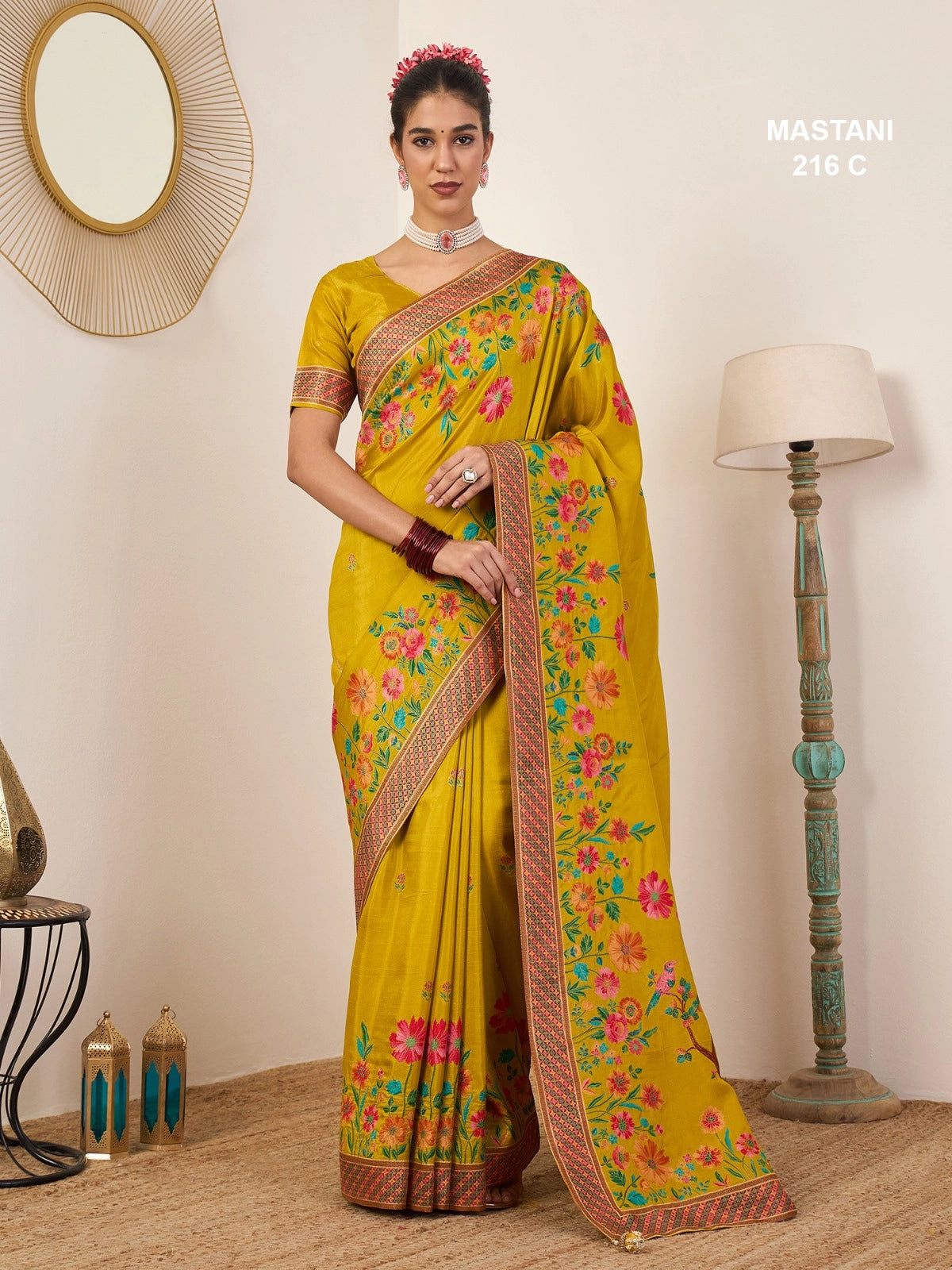 Woman wearing a yellow saree with floral patterns in a room setting.