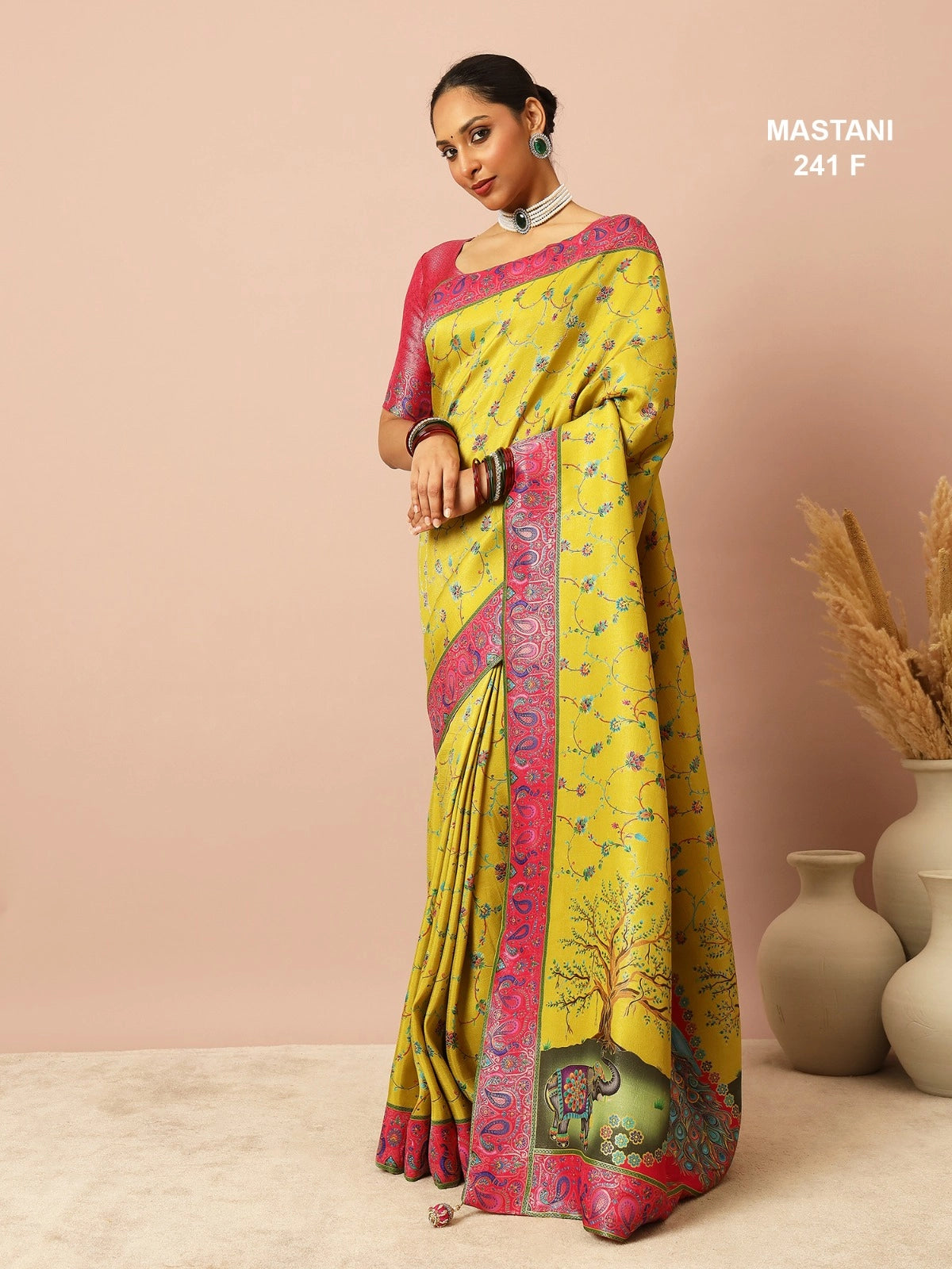 Woman wearing a yellow saree with pink border against a beige background