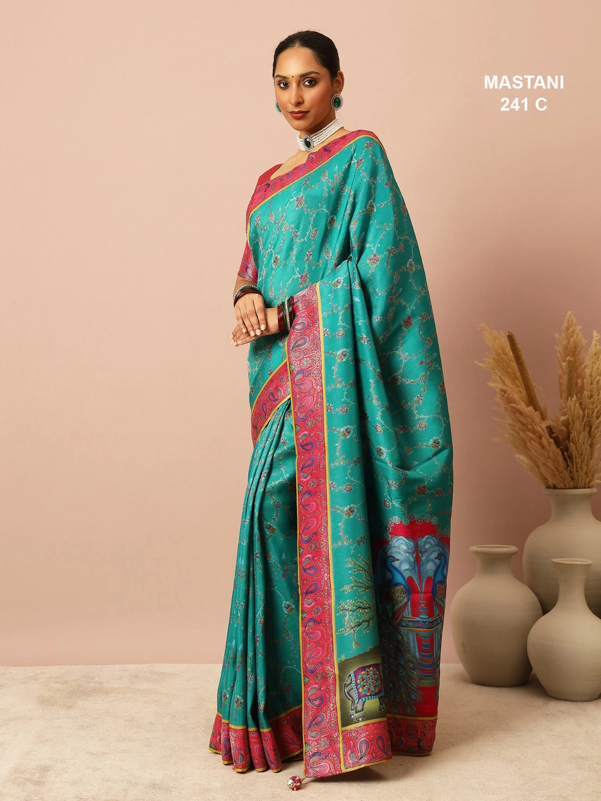 Woman wearing a teal saree with pink border against a beige background