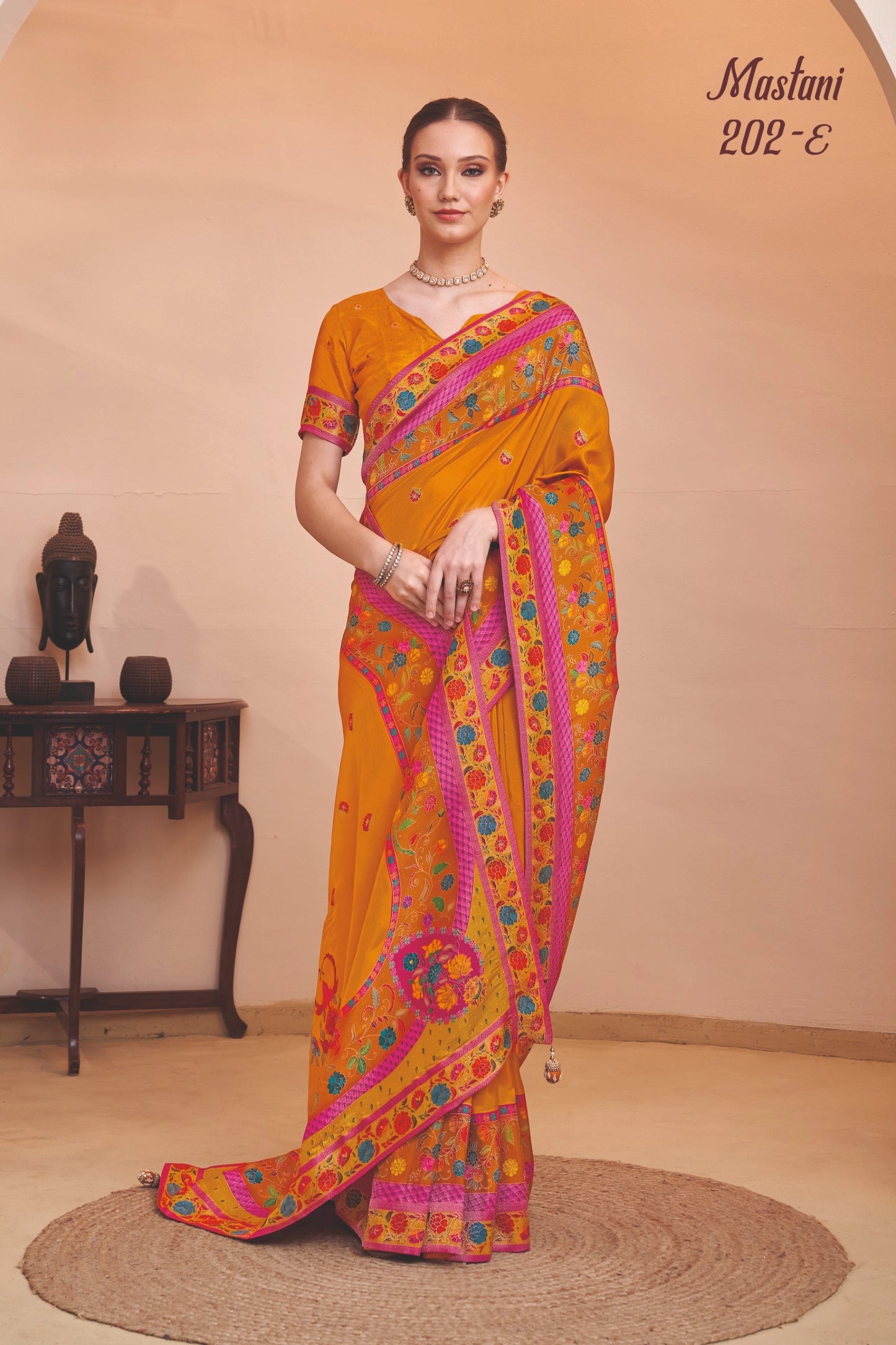 Woman wearing a bright orange saree with pink and green patterns in a room setting.