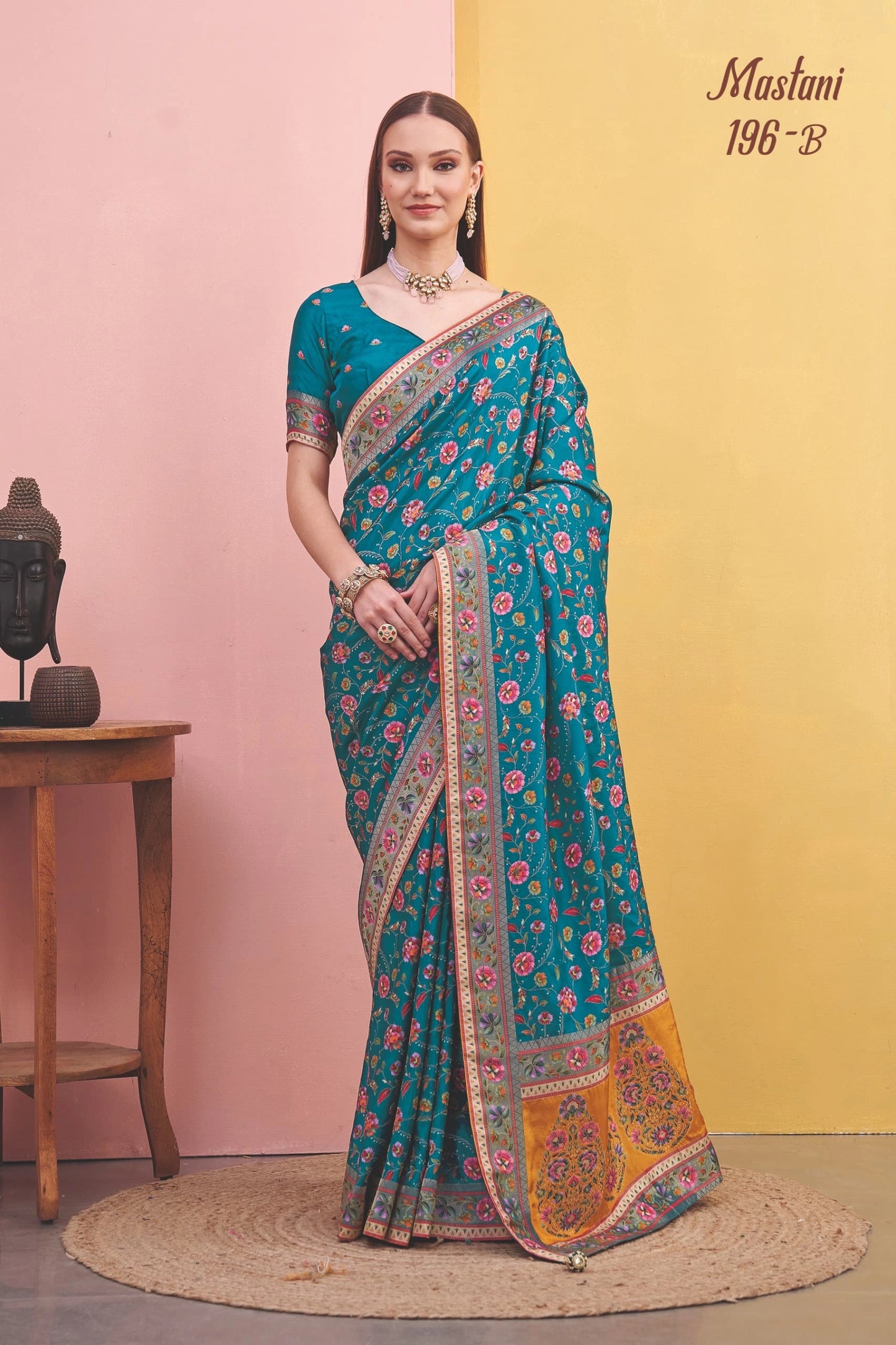 Woman wearing a teal saree with floral patterns against a pink and yellow background