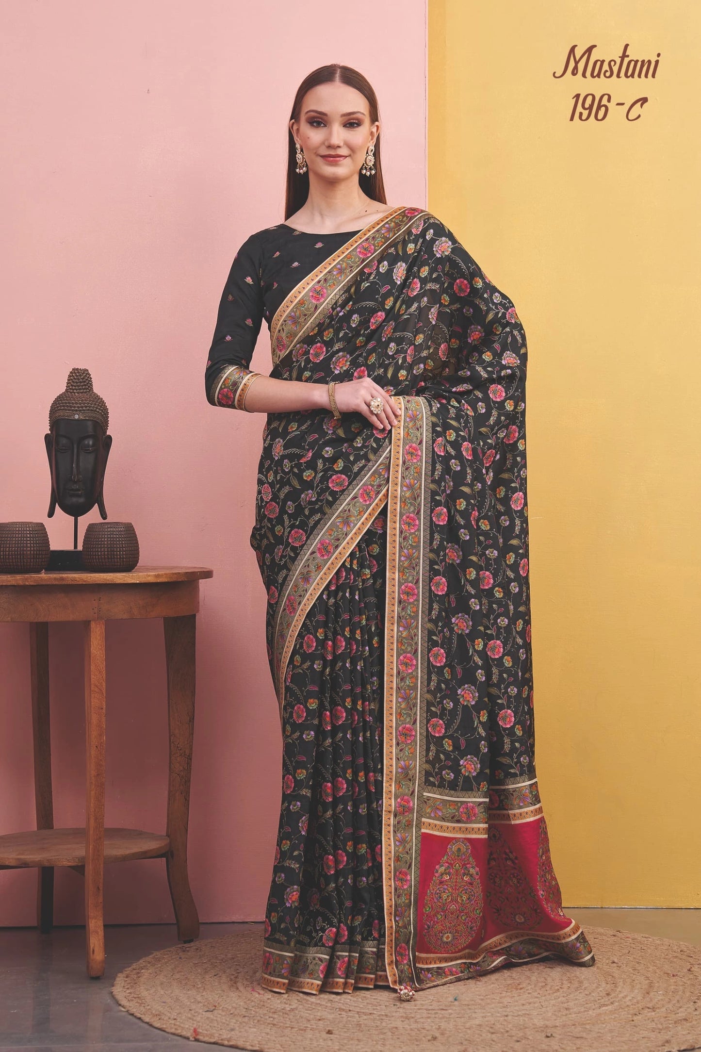 Woman wearing a black saree with floral patterns against a pink and yellow background