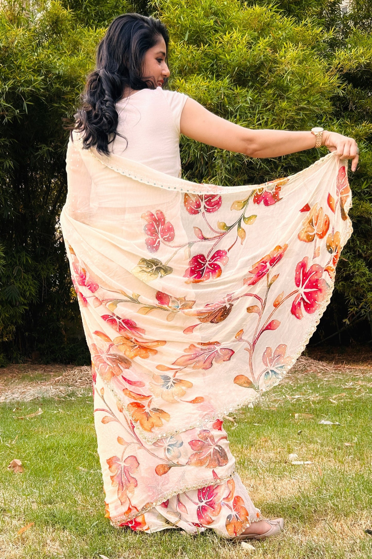 Woman wearing a floral saree outdoors with greenery in the background