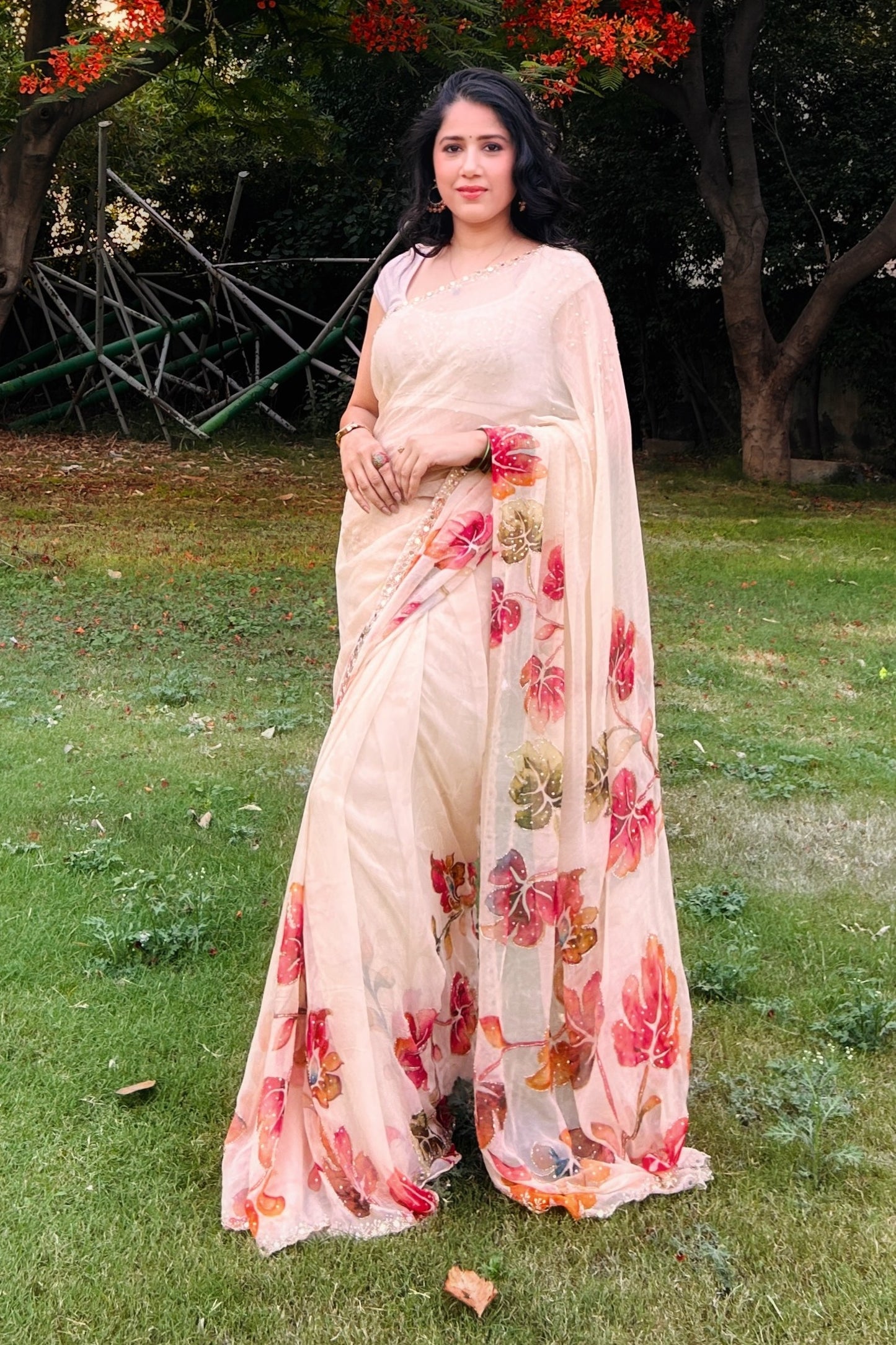 Woman in a floral saree standing outdoors on grass