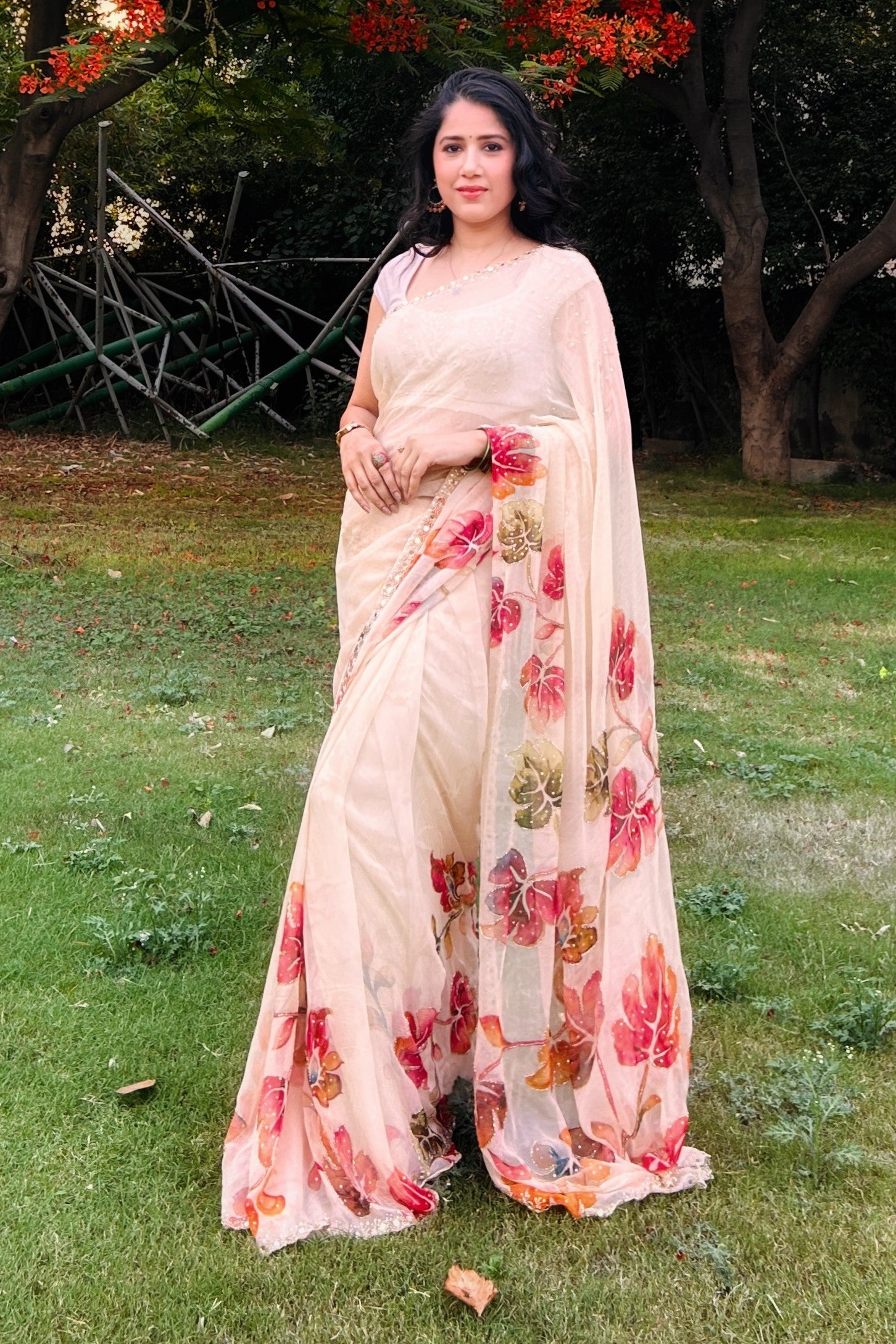 Woman in a floral saree standing outdoors on grass