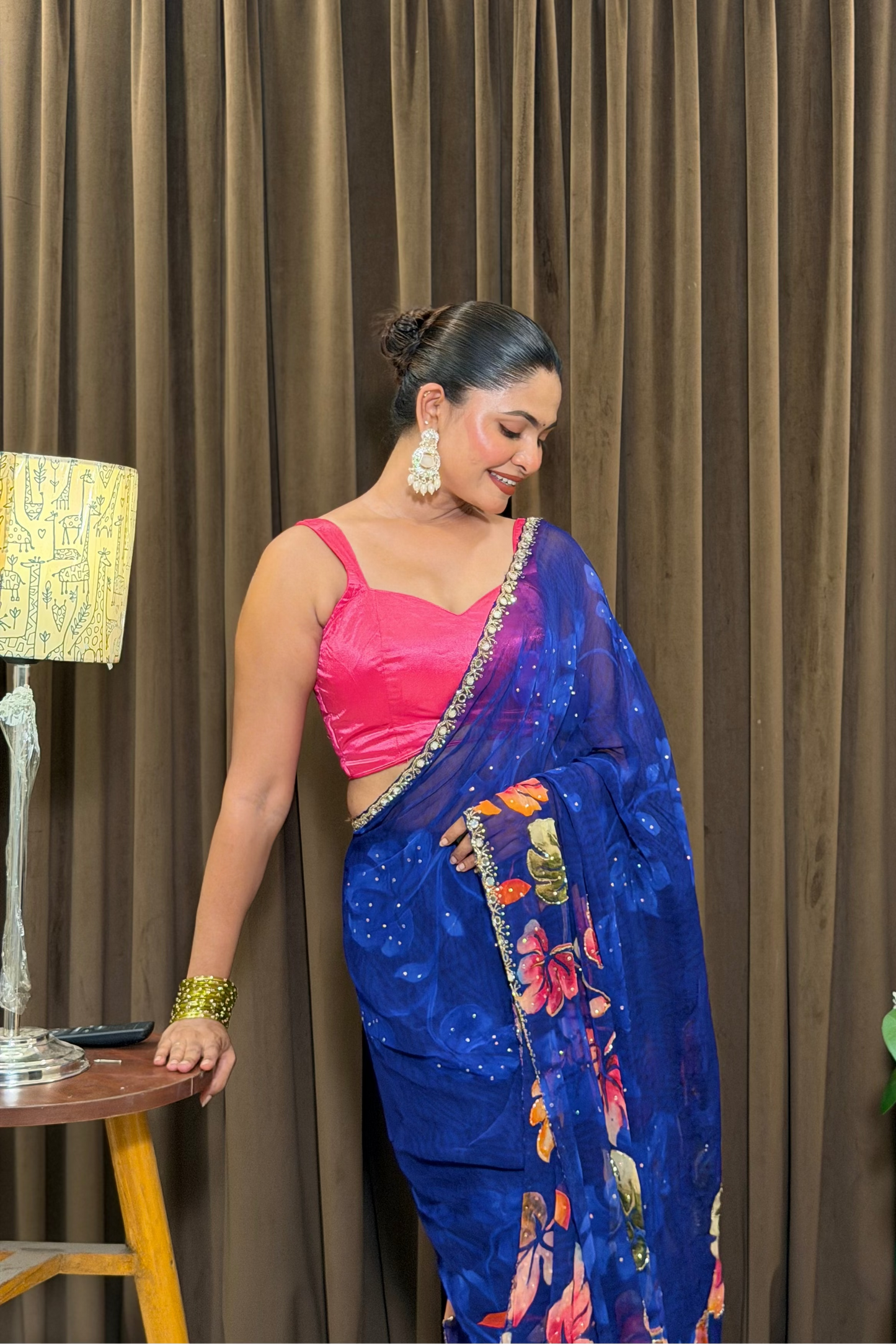 Woman in a blue saree with a pink blouse standing in front of a brown curtain.