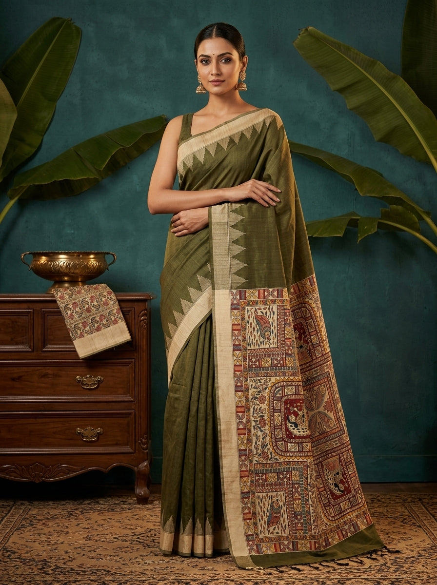 Woman wearing a green saree with a patterned border against a teal wall.