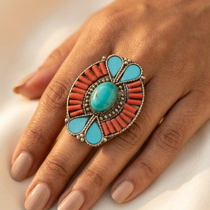 Ring with turquoise and coral stones on a hand against a neutral background