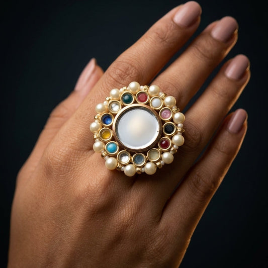 Hand wearing a decorative ring with pearls and gemstones on a dark background