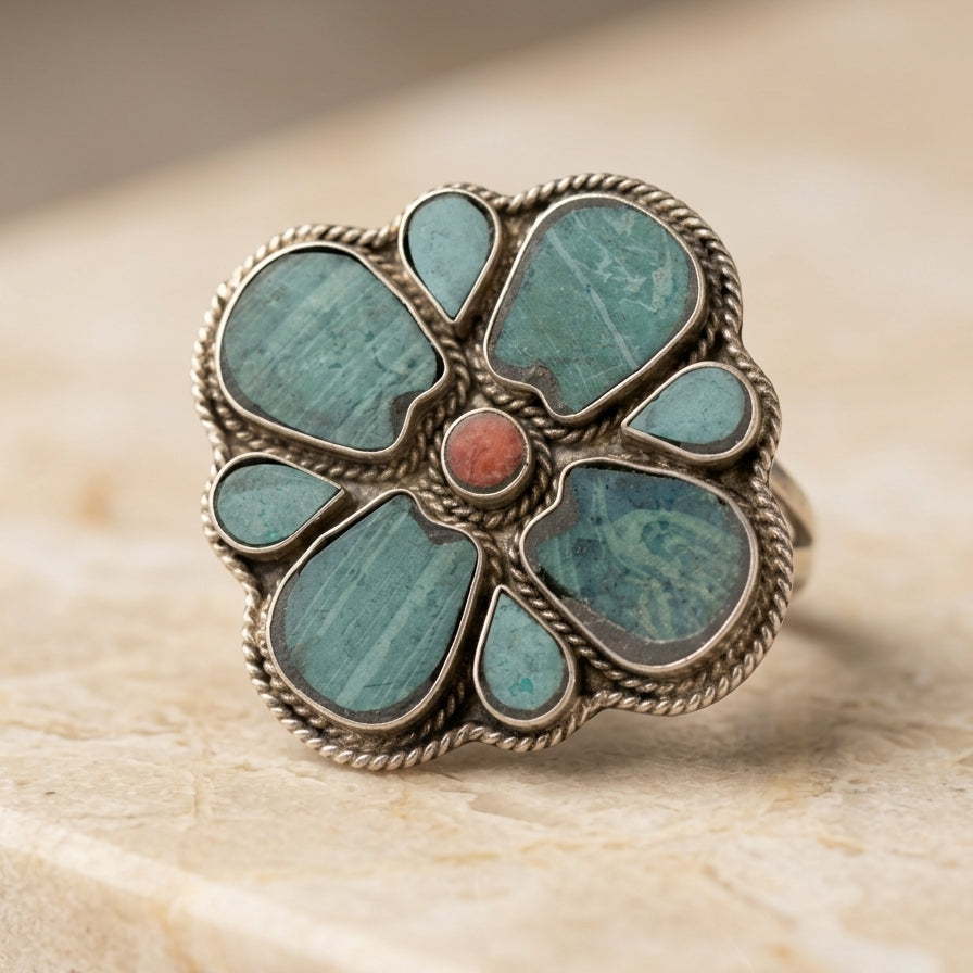 Decorative ring with turquoise stones and a red center on a beige surface