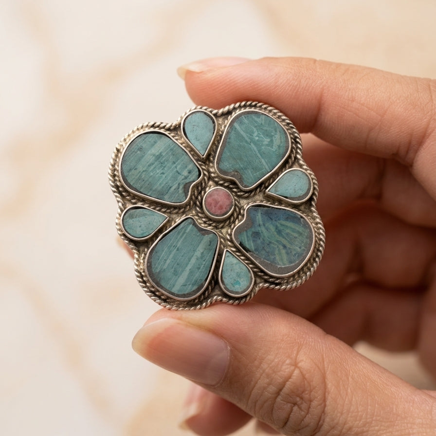 Hand holding a decorative ring with turquoise stones and a pink center.