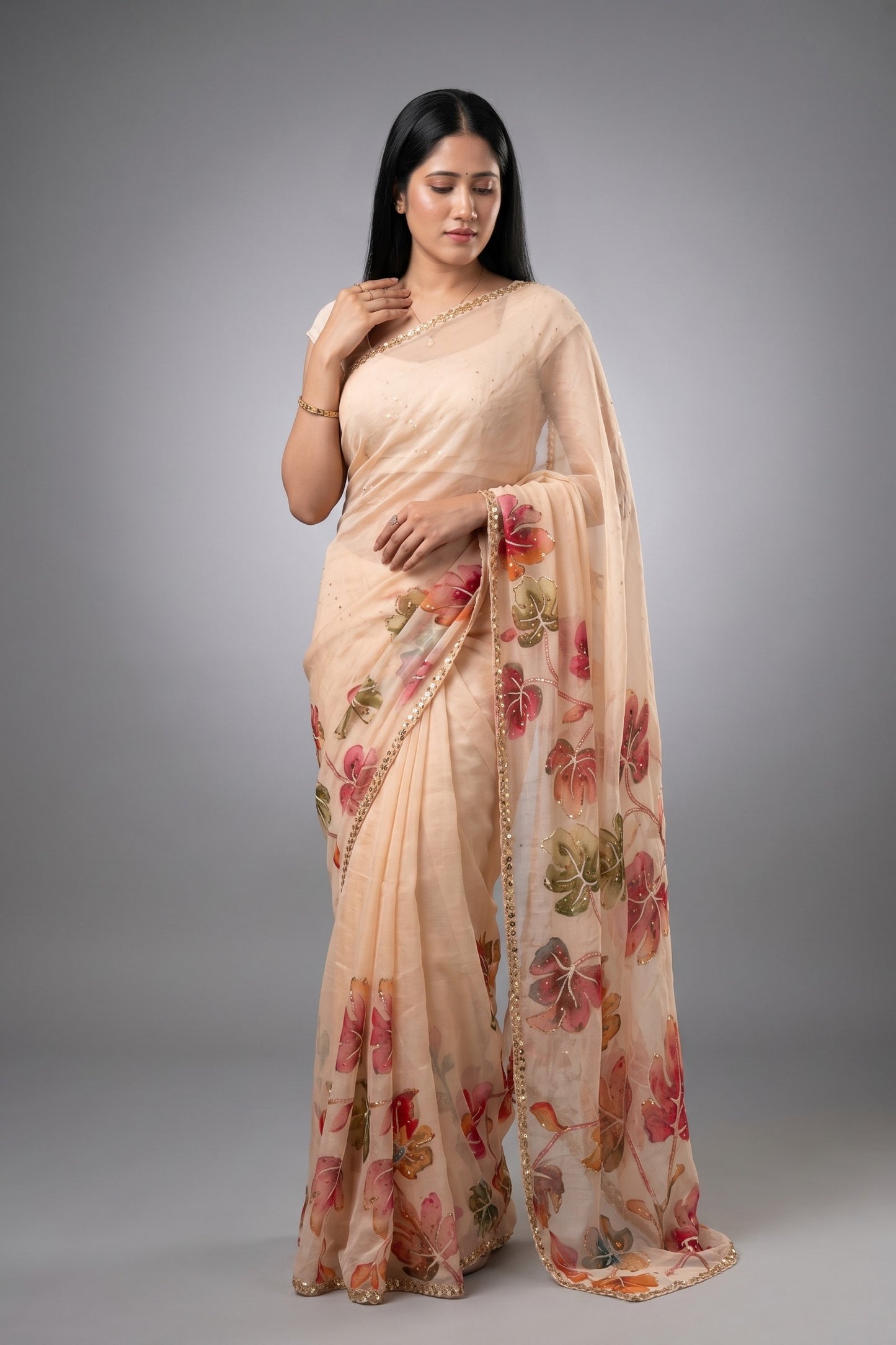 Woman wearing a beige saree with floral patterns on a gray background