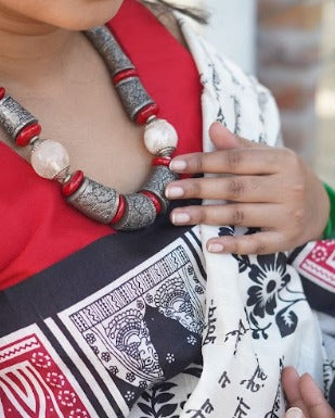 Person wearing a decorative necklace with red and silver beads, holding a patterned fabric.