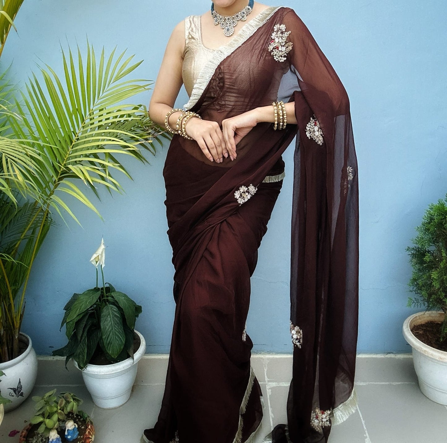 Woman wearing a brown saree with white embroidery on a beige background