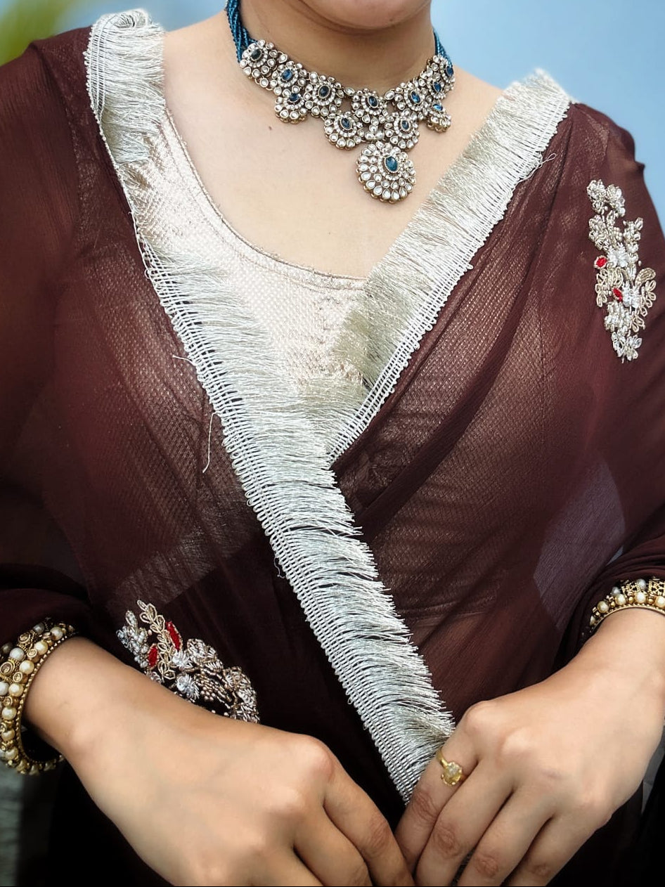Woman wearing a brown saree with white embroidery on a beige background