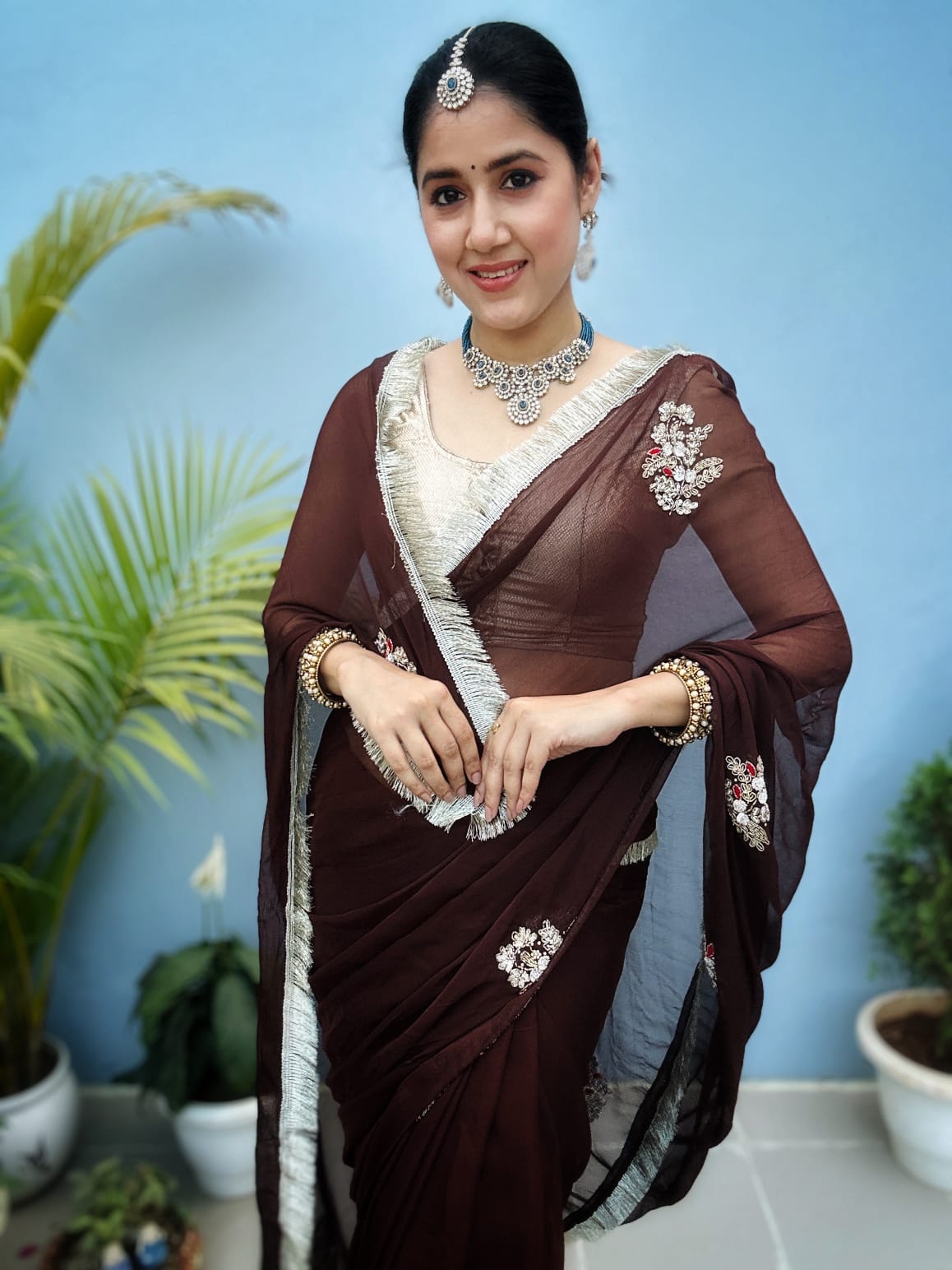 Woman wearing a brown saree with white embroidery on a beige background