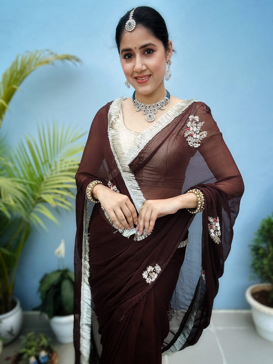 Woman wearing a brown saree with white embroidery on a beige background