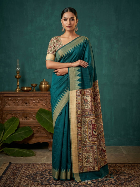 Woman wearing a teal saree with a patterned border against a teal background