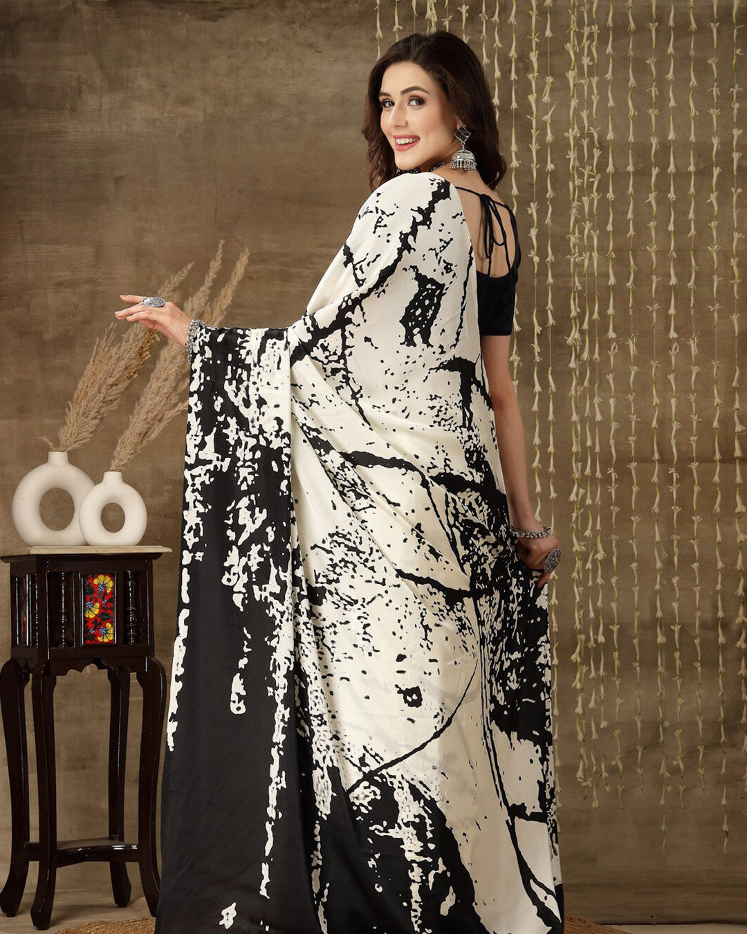 Woman wearing a black and white saree with a textured wall background