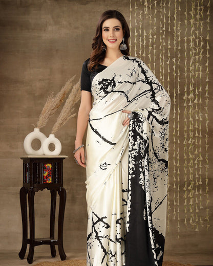 Woman wearing a white saree with black floral patterns against a textured brown background.